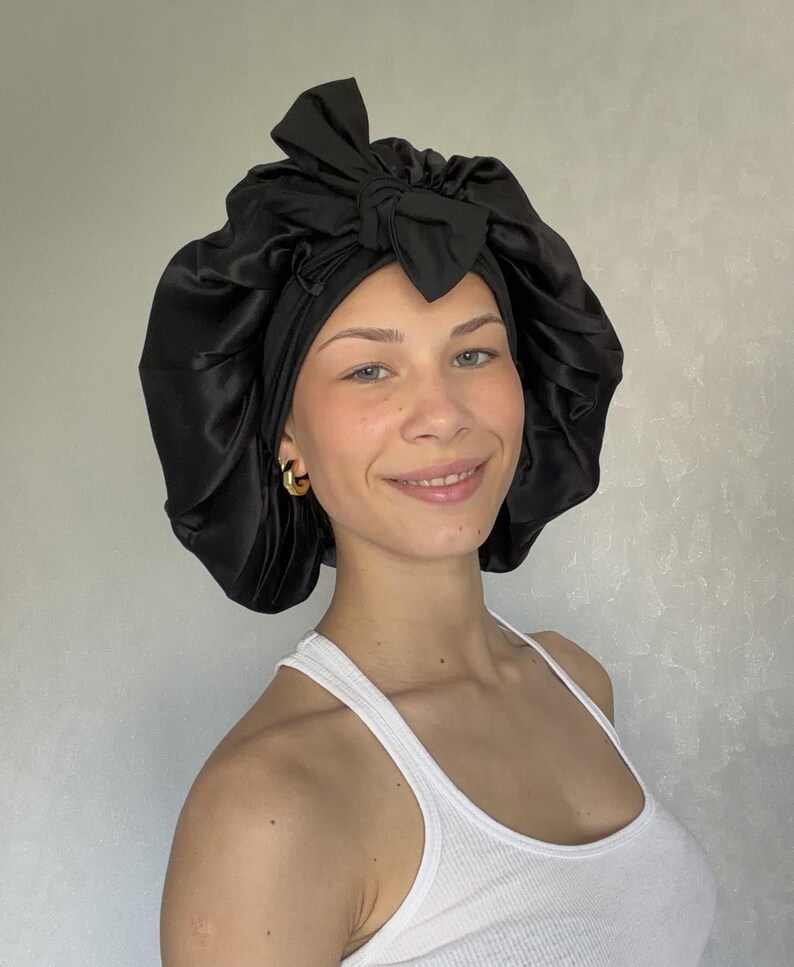 Pu&ograve; includere: Una cuffia per capelli in raso nero caratterizzata da un'ampia fascia arricciata e un fiocco decorativo annodato sul davanti. Il tessuto ha una finitura liscia e riflettente e il design include un bordo elastico per contenere i capelli.