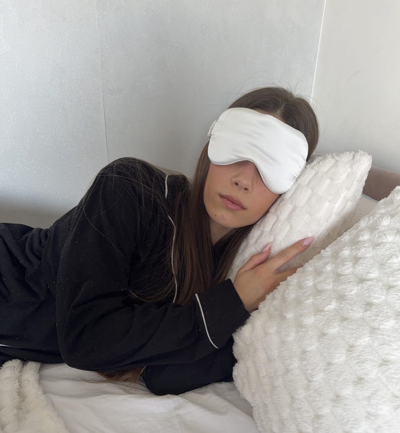 Pu&ograve; includere: Una mascherina per dormire bianca e liscia indossata sugli occhi, abbinata a una maglia da pigiama nera a maniche lunghe con sottili profili bianchi lungo il colletto e i polsini. La mascherina ha una forma semplice e sagomata.