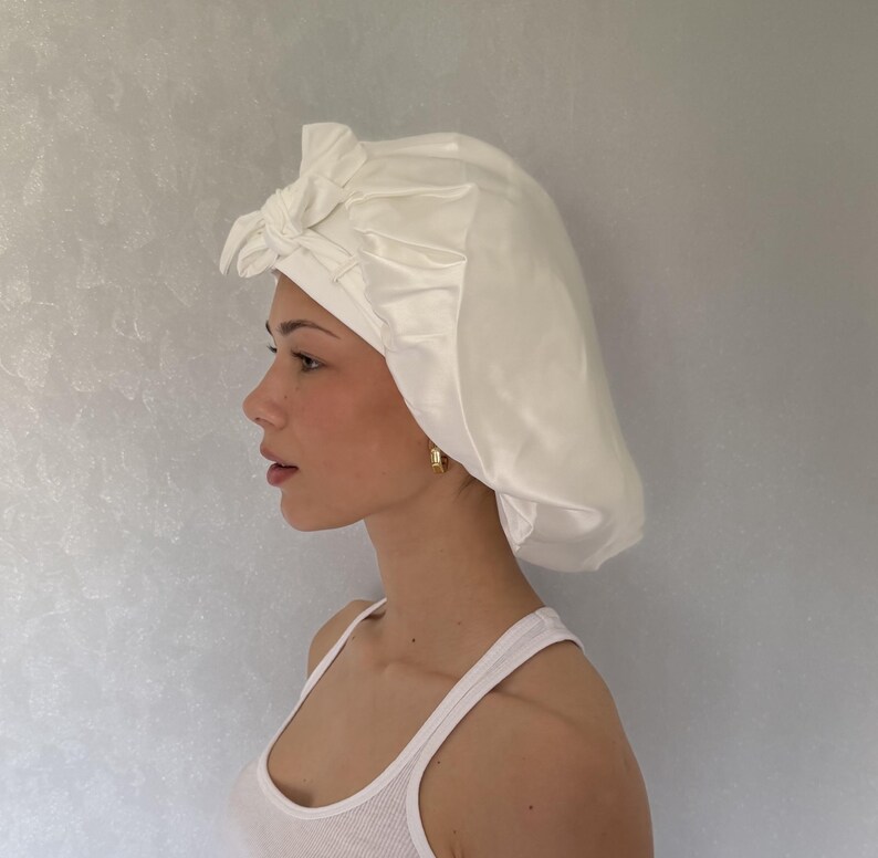 Pu&ograve; includere: Una cuffia per capelli in raso bianco caratterizzata da un design arricciato e da un dettaglio a nodo decorativo sulla parte anteriore. La cuffia ha una finitura liscia e lucente ed &egrave; realizzata con una fascia larga che aderisce alla fronte.