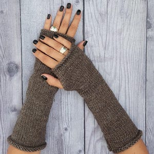 May include: A pair of brown knit fingerless gloves featuring a ribbed texture and a simple rolled hem at the wrist and finger openings. The gloves are crafted from a solid, earthy brown yarn with a consistent knit pattern throughout the design.