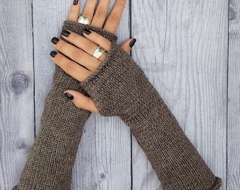 May include: A pair of brown knit fingerless gloves featuring a ribbed texture and a simple rolled hem at the wrist and finger openings. The gloves are crafted from a solid, earthy brown yarn with a consistent knit pattern throughout the design.