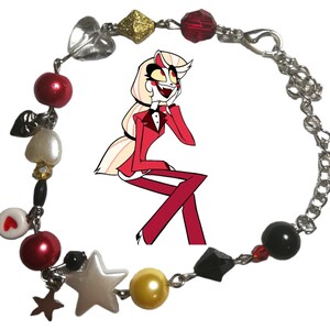 May include: A silver chain bracelet with red, white, black, and gold beads. The bracelet also features charms in the shape of hearts, stars, and a cartoon character.