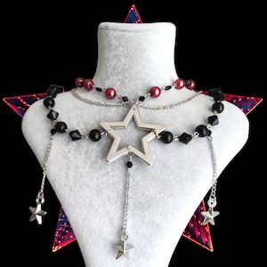 May include: A silver star pendant necklace with black and red beads. The necklace is displayed on a white mannequin bust.