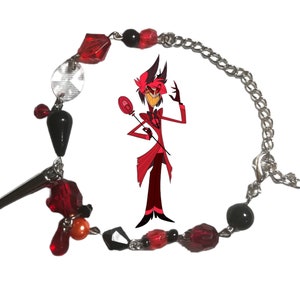 May include: A red and black beaded bracelet with a silver chain and a charm of a cartoon character. The character is red with black eyes and a black top hat. The character is holding a red and black wand.