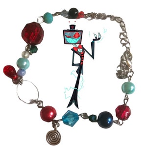 May include: A silver chain bracelet with red, blue, and green glass beads. The bracelet features a charm of a cartoon character with a television screen for a head. The character is wearing a black suit and a red bow tie.