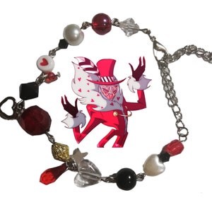 May include: A red and white charm bracelet with a heart-shaped clasp. The bracelet features a variety of charms, including hearts, stars, and a character from the animated series "Hazbin Hotel".