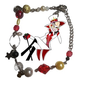May include: A red, white, and gold charm bracelet with a cartoon character charm. The character is wearing a white suit and a red hat with a crown. The bracelet has a variety of beads, including red, white, gold, and black.