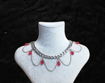 May include: A silver chain necklace with a thick curb chain and dangling red teardrop-shaped beads. The necklace is displayed on a white mannequin bust.