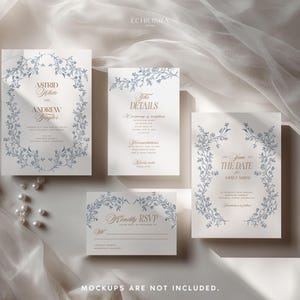 May include: A set of four white wedding stationery cards featuring blue floral vine borders and gold serif typography. The cards include an invitation, details card, save the date, and RSVP card, all arranged on a soft, draped fabric surface.