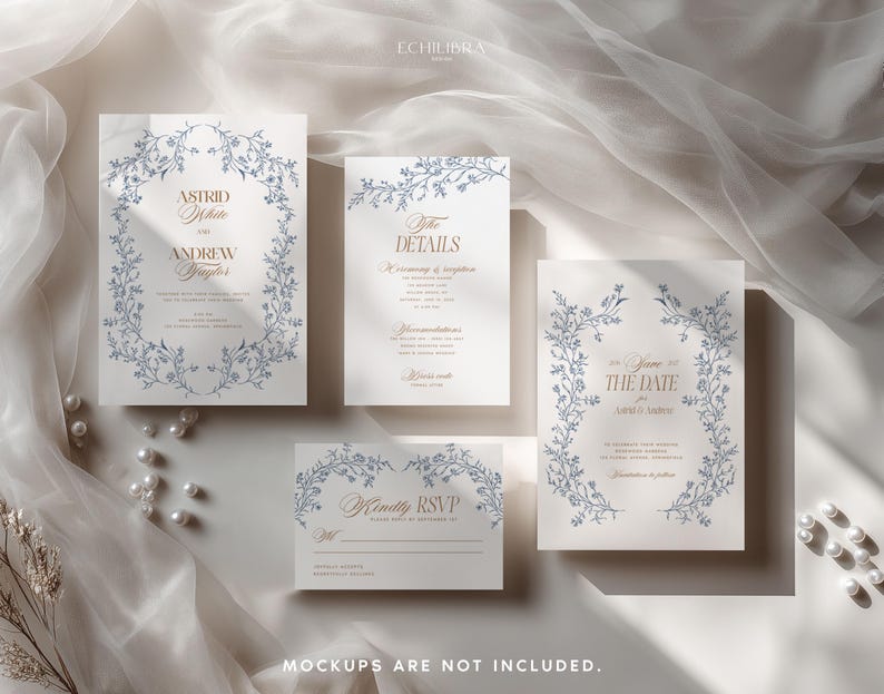 May include: A set of four white wedding stationery cards featuring blue floral vine borders and gold serif typography. The cards include an invitation, details card, save the date, and RSVP card, all arranged on a soft, draped fabric surface.