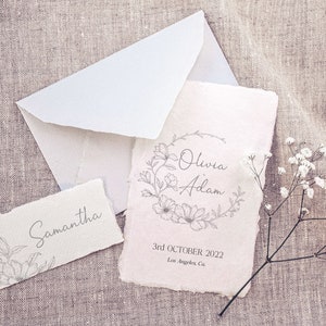 May include: A wedding invitation with a floral wreath design and the names Olivia and Adam. The date is 3rd October 2022 and the location is Los Angeles, Ca.