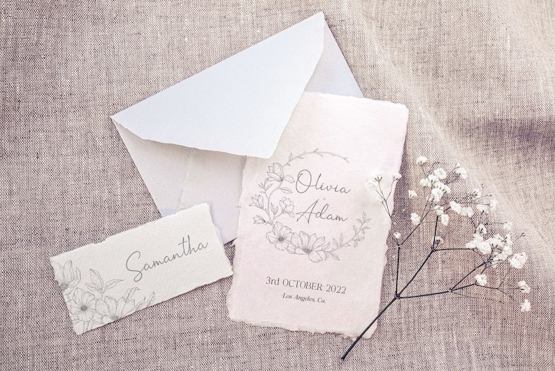 May include: A wedding invitation with a floral wreath design and the names Olivia and Adam. The date is 3rd October 2022 and the location is Los Angeles, Ca.