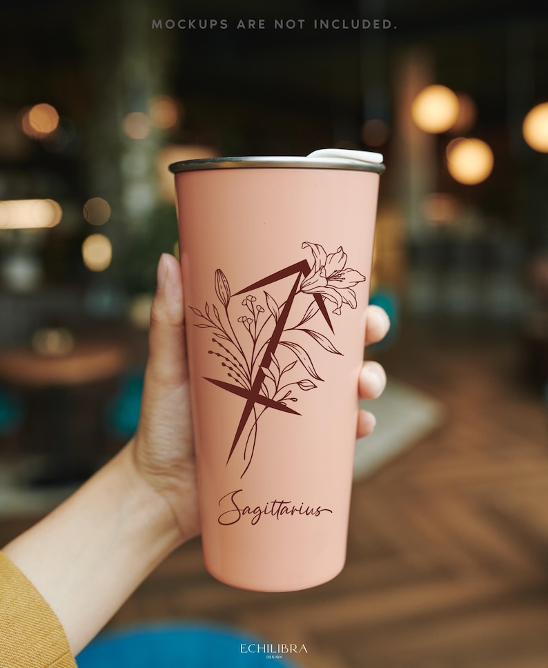 Puede incluir: Un vaso de acero inoxidable rosa con un dise&ntilde;o floral y el signo del zod&iacute;aco Sagitario. El vaso tiene una tapa negra y un interior blanco.