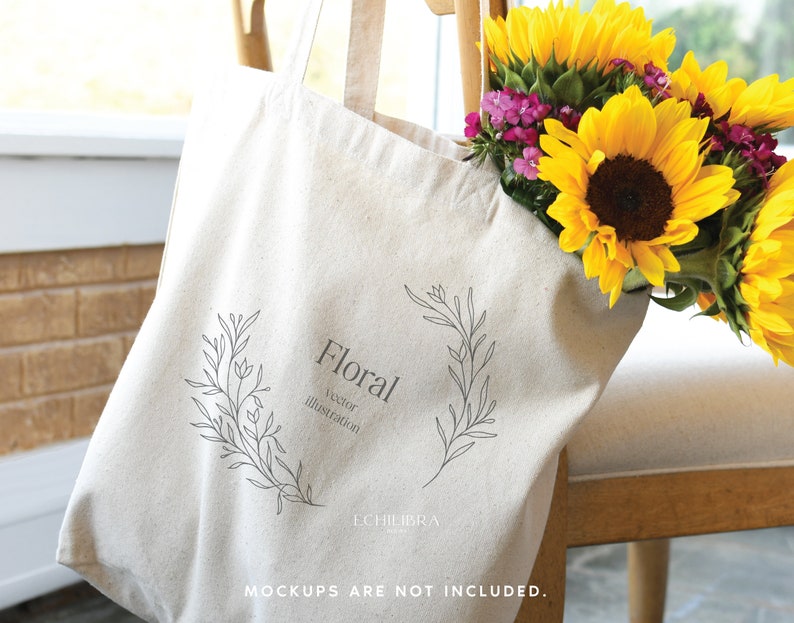May include: A beige tote bag with a floral illustration and the word "Floral". The bag is filled with bright yellow sunflowers and small purple flowers. The bag is resting on a wooden chair.