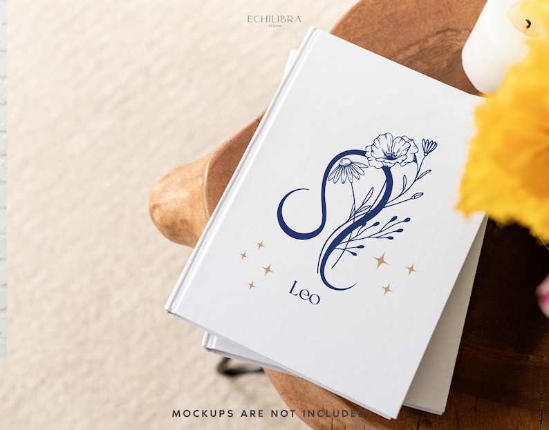 Puede incluir: Un diario blanco con un dise&ntilde;o floral azul y dorado que representa el signo del zod&iacute;aco Leo. El diario tiene el texto "Leo" impreso en la portada.