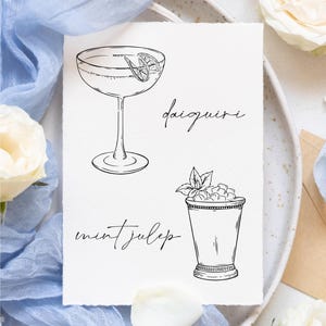 May include: A printable digital download of two cocktail illustrations. The first illustration is a daiquiri in a martini glass with a lime wedge. The second illustration is a mint julep in a silver cup with mint leaves and ice. The text "Mockups are not included." is at the bottom of the page.