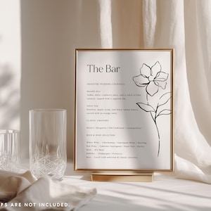 Puede incluir: Un letrero rectangular en un marco dorado con el texto The Bar, una lista de c&oacute;cteles de boda, bebidas cl&aacute;sicas y selecci&oacute;n de cervezas y vinos, acompa&ntilde;ado de un dibujo lineal negro de una flor sobre un fondo blanco.