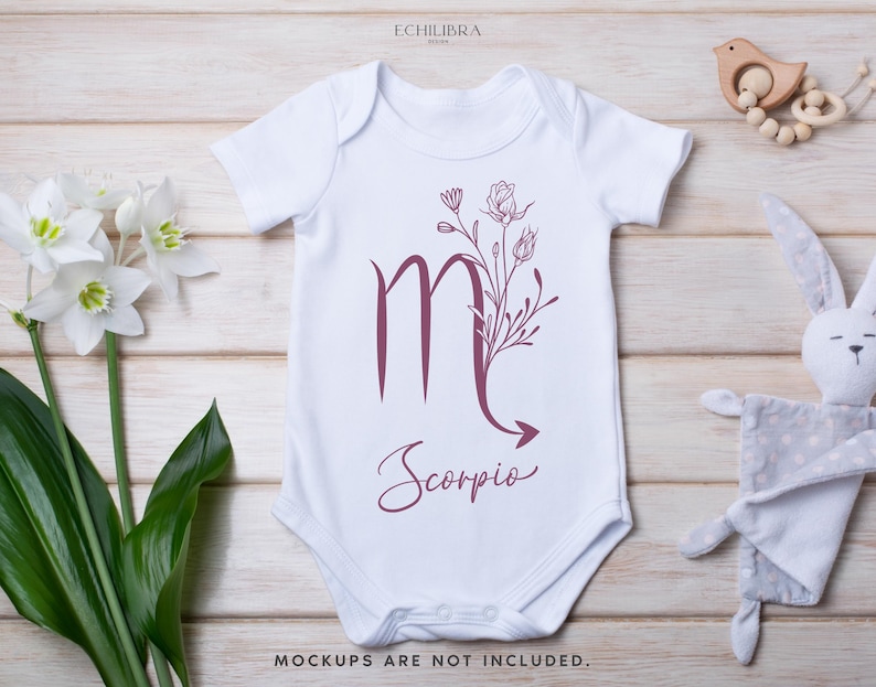 Puede incluir: Un body blanco para beb&eacute; con un dise&ntilde;o floral burdeos y el s&iacute;mbolo del zod&iacute;aco de Escorpio. El texto "Scorpio" est&aacute; escrito en cursiva debajo del s&iacute;mbolo.