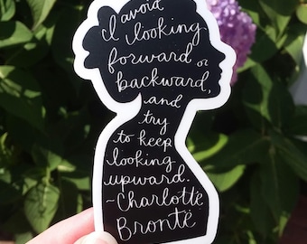 Puede incluir: Pegatina en blanco y negro con una silueta de cabeza de mujer y la cita "Evita mirar hacia adelante o hacia atrás, y trata de mantener la mirada hacia arriba. -Charlotte Brontë"