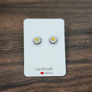 May include: A pair of white daisy flower stud earrings with yellow centers on a white card with the text "Handmade with love" and a red heart.