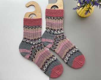 May include: A pair of knitted socks with a pink, gray, and beige striped pattern. The socks are displayed on wooden hangers.