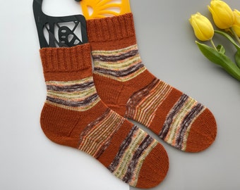 May include: A pair of brown and beige striped socks with a subtle green and brown color variation. The socks are knitted and have a soft, comfortable texture.