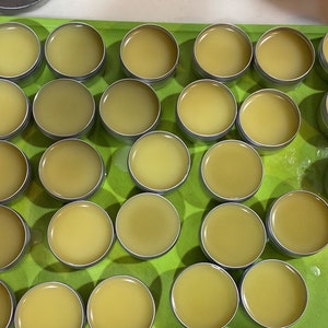 May include: A green tray filled with 24 small round containers of yellow balm. The containers are arranged in a grid pattern.
