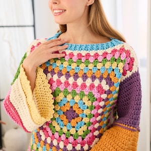 May include: A colorful crochet sweater with a square pattern in various colors, including pink, yellow, blue, and orange. The sweater has a boat neck and bell sleeves. The sleeves are a mix of colors, with a solid purple sleeve and an orange sleeve.