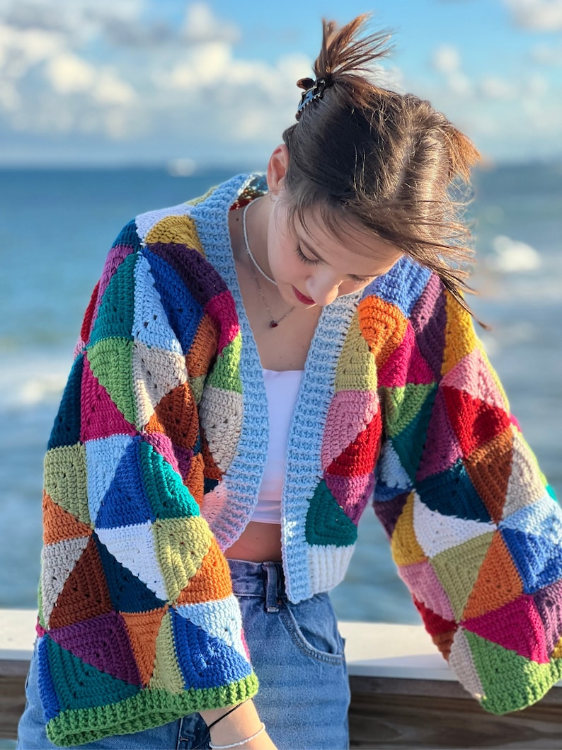 May include: A colorful crocheted cardigan with a patchwork design. The cardigan is cropped and has long sleeves. The cardigan is made with a variety of colors, including red, orange, yellow, green, blue, and purple.