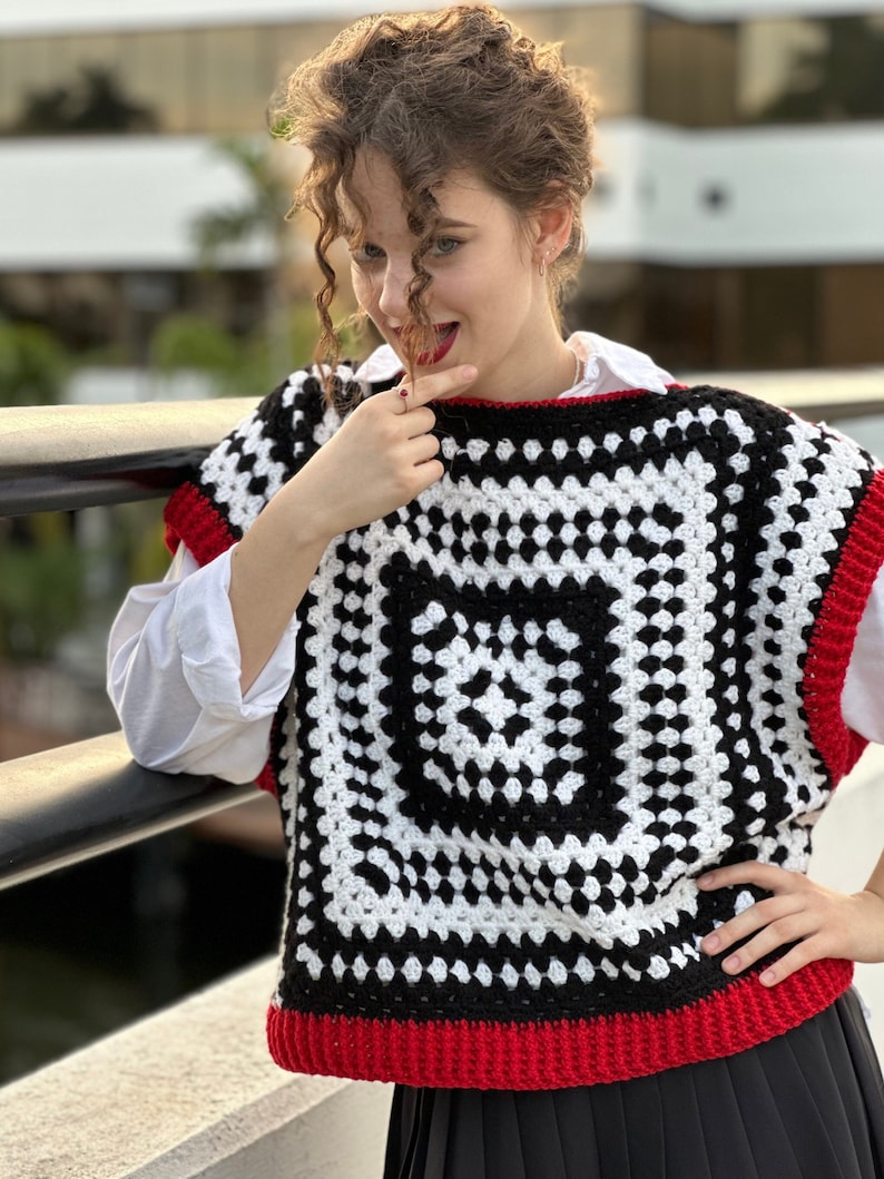 May include: A black and white crochet vest with a red trim. The vest is sleeveless and has a square pattern.
