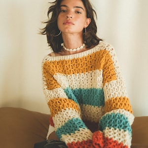 May include: A multi-colored striped crochet sweater with a loose fit and long sleeves. The sweater is made of a soft, lightweight yarn and features a relaxed, bohemian style.