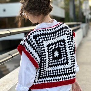 May include: A black and white crochet vest with red trim. The vest has a square pattern with a smaller square in the center.