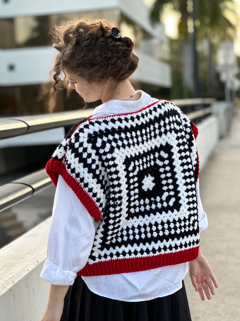 May include: A black and white crochet vest with red trim. The vest has a square pattern with a smaller square in the center.