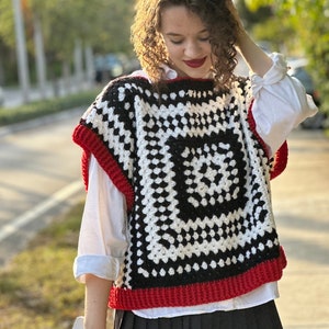 May include: A black and white crochet vest with a red trim. The vest has a square pattern with a smaller square in the center.