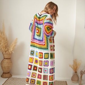 Può includere: Un lungo cardigan bianco all'uncinetto con un motivo a quadrati della nonna colorati. Il cardigan ha un collo a V e maniche lunghe.