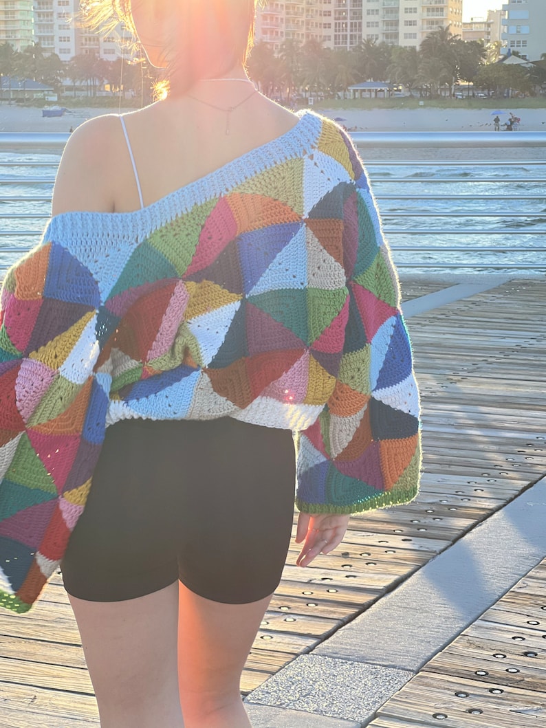 May include: A colorful crochet sweater with a geometric pattern. The sweater is made with a variety of colors, including blue, green, red, yellow, and white. The sweater has a loose fit and a wide neckline.