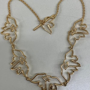 May include: A gold necklace with a chain and a series of connected, open-work, bird-shaped pendants.
