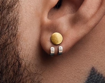 May include: A close-up of an ear with a gold-colored, circular earring and silver-colored, rectangular earring. The earring is a plug style. The person has a beard and a tattoo on their neck.
