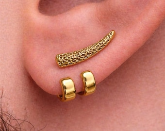 May include: Gold-colored ear jewelry set. The set includes a textured, curved ear cuff and two small hoop earrings. The jewelry is displayed on an ear, showcasing the design and fit. The earrings have a polished finish.