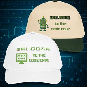 Può includere: Due cappellini da baseball. Uno è bianco con testo verde e una grafica di computer, l'altro è beige con una visiera verde e una grafica di robot. Entrambi i cappellini hanno il testo "WELCOME to the code cove" e "WELCOME to the code cave".