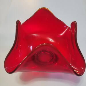 May include: A red glass bowl with a wavy, organic shape. The bowl has a smooth, glossy finish and a slightly flared rim.