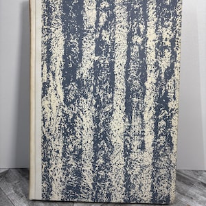 Op de afbeelding: Een vintage hardcover boek met een blauw en wit abstract ontwerp op de kaft. De kaft heeft een textuur en een verweerde uitstraling.