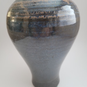 May include: A dark blue ceramic vase with a flared opening and a rounded bottom. The vase has a glossy finish with subtle brown streaks.