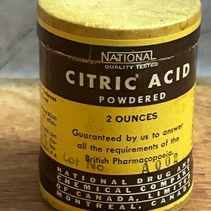 以下が含まれることがあります： 黄色と茶色の段ボール製の容器で、ラベルには「National Quality Tested Citric Acid Powdered 2 Ounces Guaranteed by us to answer all the requirements of the British Pharmacopoeia. Lot No A002 National Drug and Chemical Company of Canada, Limited Montreal, Canada」と記載されています。