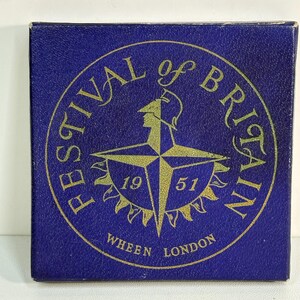 May include: A navy blue box featuring a gold circular emblem for the Festival of Britain. The emblem includes a compass rose design and the year "1951". The text "WHEEN LONDON" is printed below the emblem in gold.
