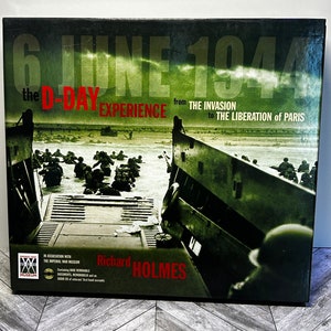 Può includere: Una fotografia in bianco e nero di soldati che sbarcano su una spiaggia durante la seconda guerra mondiale. L'immagine è tratta da un libro intitolato "6 giugno 1944: L'esperienza del D-Day dall'invasione alla liberazione di Parigi" di Richard Holmes. Il libro è in collaborazione con l'Imperial War Museum.