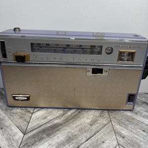 May include: Vintage Roxy transistor radio in a lavender and silver color scheme. The radio features a speaker grill, tuning dial, and the text "TRANSISTOR". The radio has a "SUPER SENSITIVE" label.