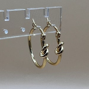 May include: Gold hoop earrings with a knot design.