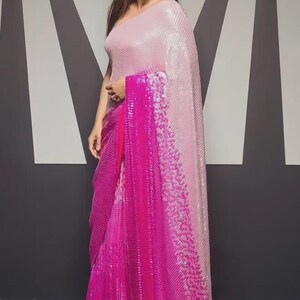 May include: A woman wearing a pink and fuchsia sequined saree. The saree features a gradient effect, transitioning from light pink to a vibrant fuchsia. The fabric has a textured, shimmering appearance, and the design is elegant and eye-catching.