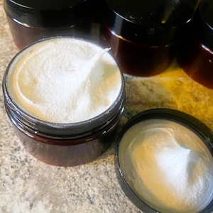 Puede incluir: Varios frascos peque&ntilde;os de color marr&oacute;n oscuro con tapas negras, llenos de una sustancia cremosa blanca. Un frasco est&aacute; abierto, revelando la textura del producto. Los frascos est&aacute;n dispuestos sobre una superficie clara.